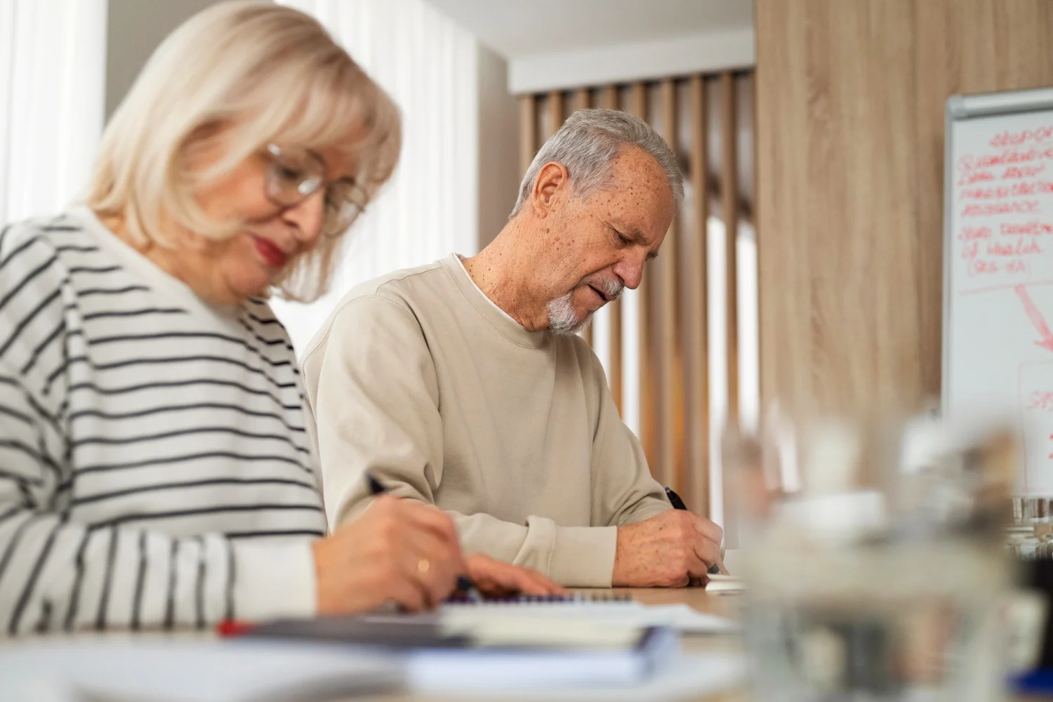 Dos personas mayores firmando documentos en una mesa